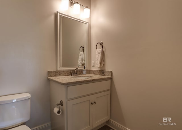 half bathroom with toilet, vanity, and baseboards