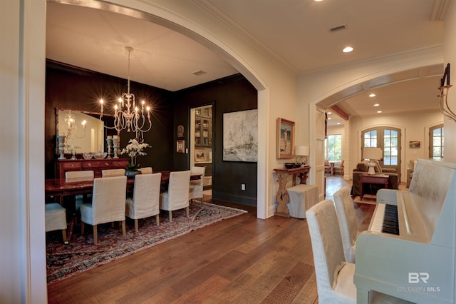 dining space with visible vents, crown molding, wood finished floors, arched walkways, and a notable chandelier