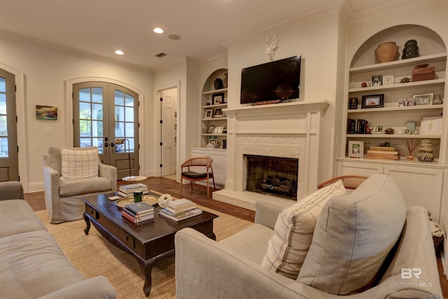 living room featuring ornamental molding, built in features, a high end fireplace, french doors, and light wood-style floors