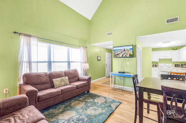 living area featuring light wood-style floors, visible vents, high vaulted ceiling, and baseboards