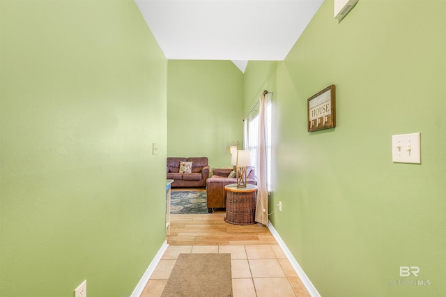 hallway with lofted ceiling, baseboards, and light tile patterned floors