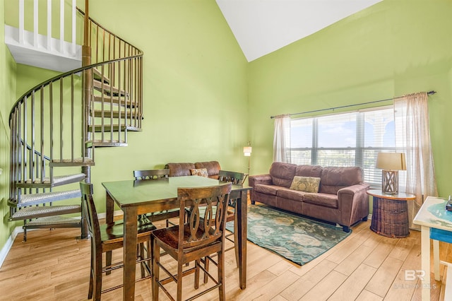 dining room featuring light wood-style floors, baseboards, stairs, and high vaulted ceiling