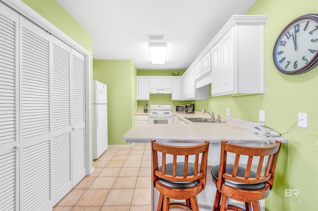 kitchen featuring white appliances, a breakfast bar area, a peninsula, light countertops, and a sink