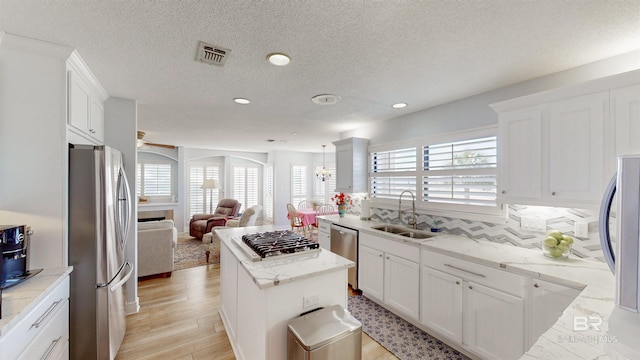 kitchen with visible vents, open floor plan, stainless steel appliances, white cabinetry, and a sink