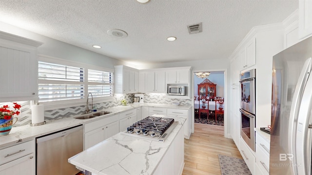 kitchen with visible vents, a center island, white cabinets, stainless steel appliances, and a sink