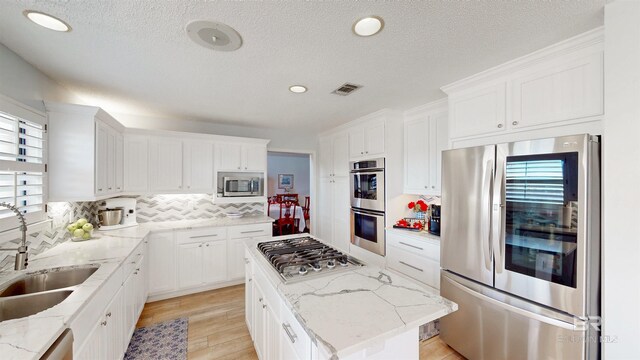 kitchen featuring visible vents, a kitchen island, a sink, stainless steel appliances, and white cabinets