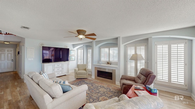 living room with visible vents, light wood-style floors, ceiling fan, and a tile fireplace