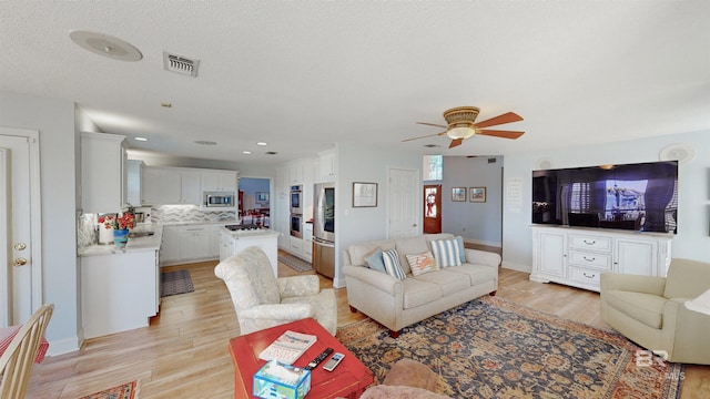 living area with light wood-type flooring, baseboards, visible vents, and ceiling fan