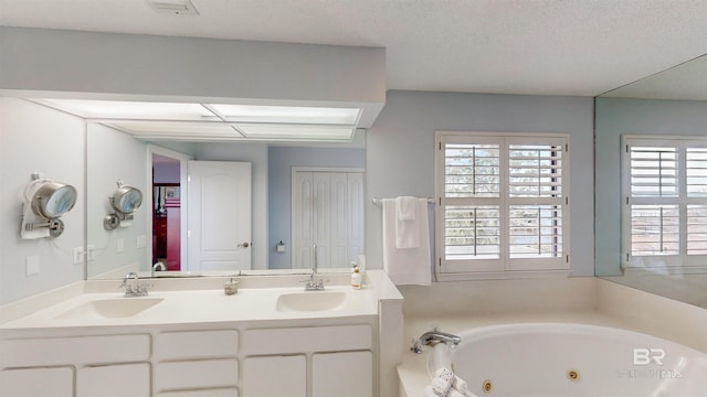 full bath with double vanity, a tub with jets, a textured ceiling, and a sink