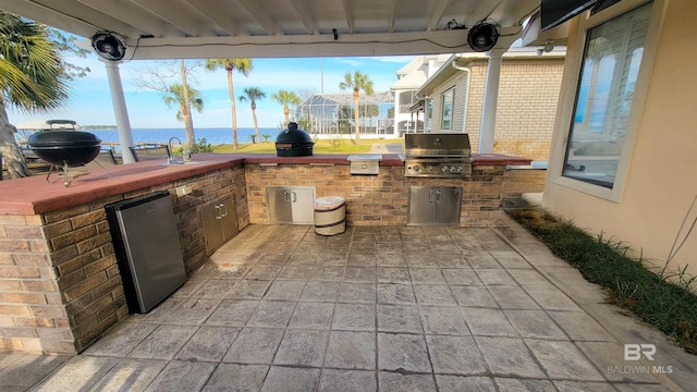 view of patio / terrace with a water view, glass enclosure, an outdoor kitchen, a grill, and a sink