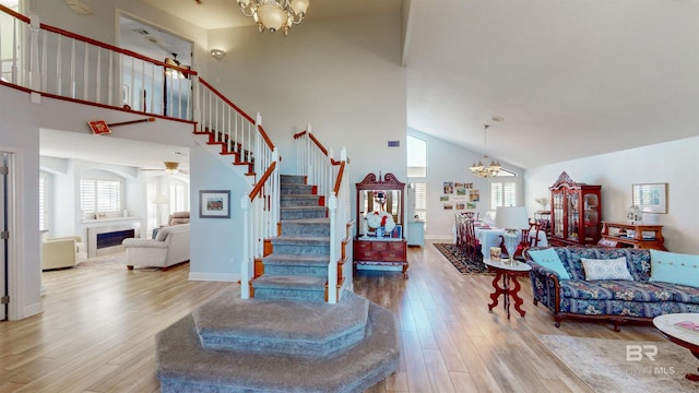 stairs featuring baseboards, ceiling fan with notable chandelier, a fireplace, a towering ceiling, and wood finished floors