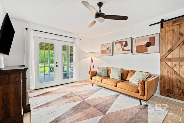 living room featuring french doors, light hardwood / wood-style flooring, a textured ceiling, ceiling fan, and a barn door