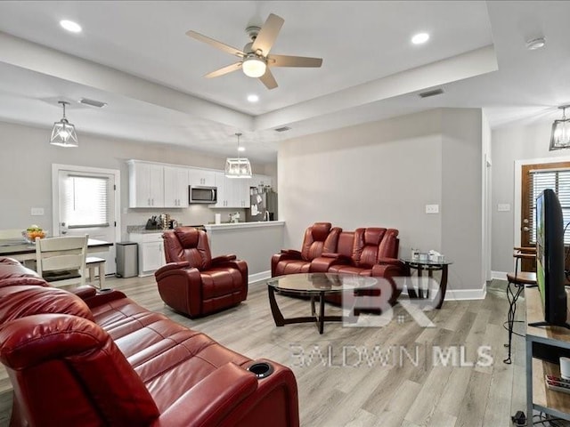 living room featuring ceiling fan, a tray ceiling, and light hardwood / wood-style flooring