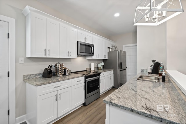 kitchen with hanging light fixtures, sink, white cabinetry, light stone counters, and stainless steel appliances