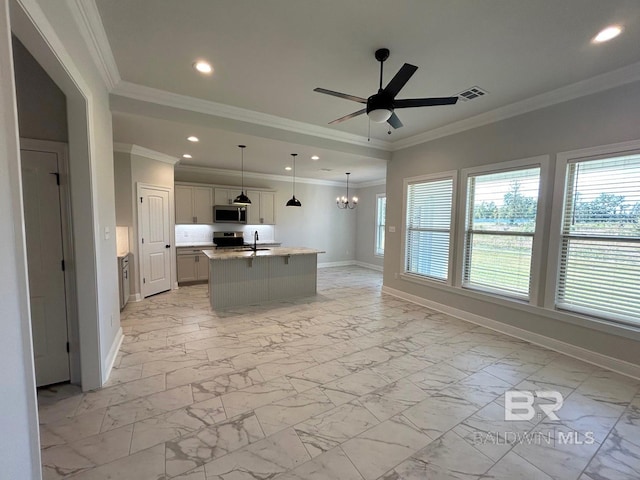 kitchen featuring light stone counters, ornamental molding, stainless steel appliances, decorative light fixtures, and an island with sink