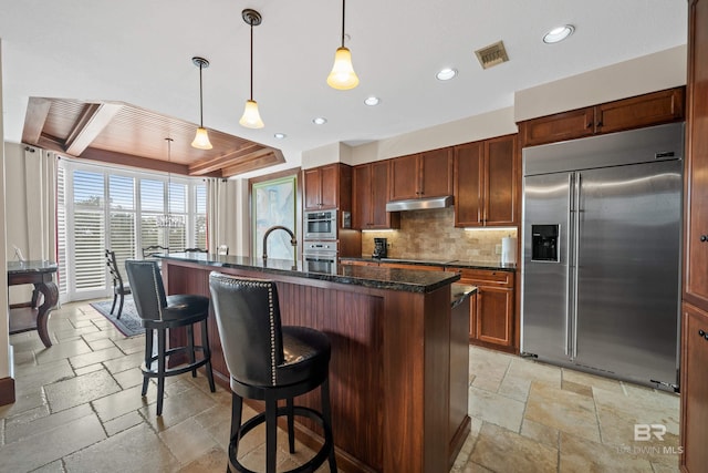 kitchen featuring built in fridge, decorative light fixtures, decorative backsplash, a breakfast bar, and a center island with sink