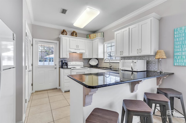 kitchen featuring light tile patterned flooring, under cabinet range hood, a peninsula, white appliances, and a sink