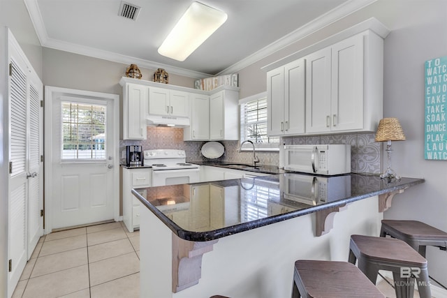 kitchen with under cabinet range hood, a peninsula, white appliances, a sink, and white cabinetry