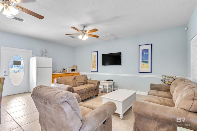 living area featuring light tile patterned floors, a textured ceiling, a ceiling fan, and attic access