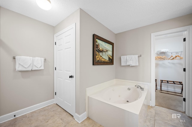 bathroom featuring a textured ceiling, a tub with jets, tile patterned floors, and baseboards