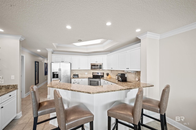 kitchen featuring appliances with stainless steel finishes, a raised ceiling, decorative backsplash, and a kitchen bar