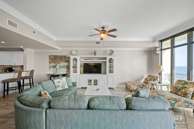 living room with crown molding, a textured ceiling, visible vents, and wood finished floors