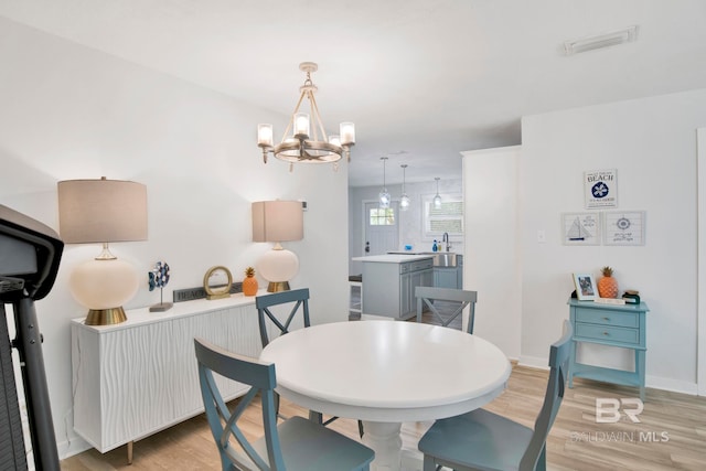 dining room featuring light wood finished floors, visible vents, a notable chandelier, and baseboards