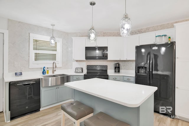 kitchen with a breakfast bar area, light wood-style flooring, a sink, light countertops, and black appliances