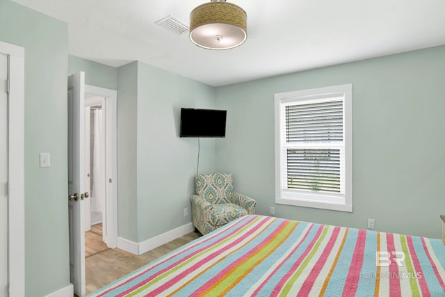 bedroom with baseboards, visible vents, and wood finished floors