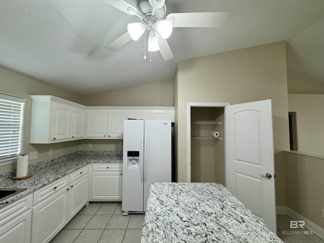 kitchen with white refrigerator with ice dispenser, lofted ceiling, white cabinets, light tile patterned flooring, and light stone countertops