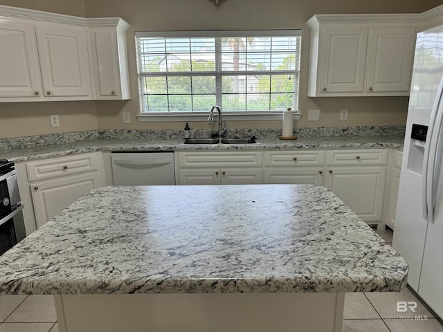 kitchen with white appliances, a kitchen island, white cabinetry, and a sink