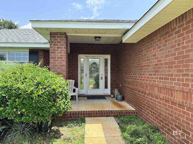 entrance to property featuring roof with shingles and brick siding