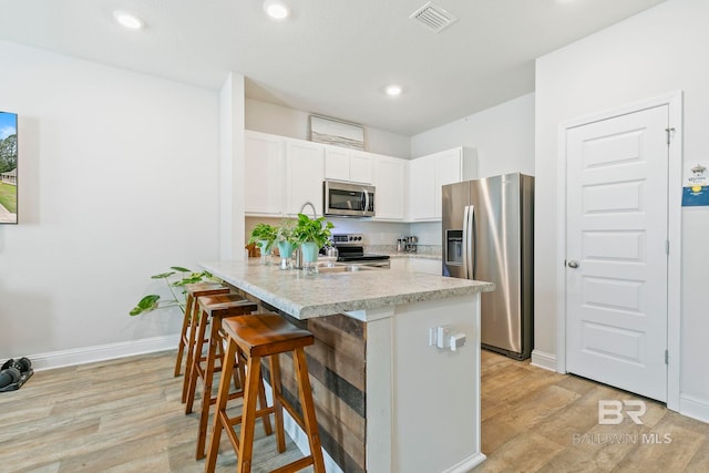 kitchen with a kitchen breakfast bar, light hardwood / wood-style flooring, white cabinets, and stainless steel appliances