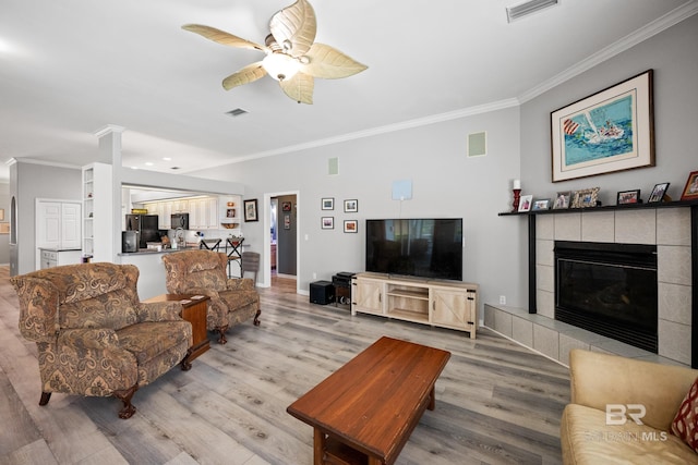 8585 Bay Harbor Rd, Elberta, AL 36530 - living room with crown molding, light wood-style flooring, ceiling fan, and a tiled fireplace