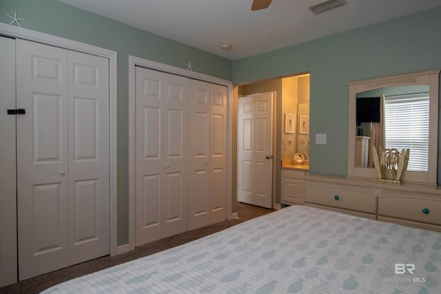 bedroom with multiple closets, dark colored carpet, visible vents, and a ceiling fan