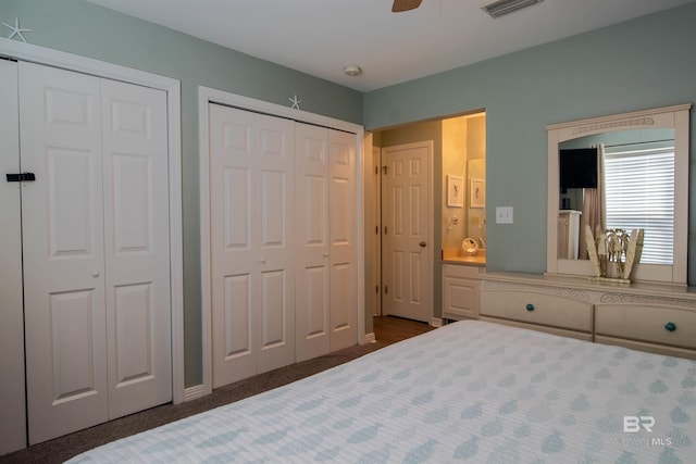 bedroom featuring ceiling fan, dark colored carpet, two closets, and visible vents