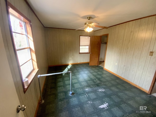 unfurnished room featuring wooden walls, ceiling fan, a healthy amount of sunlight, and ornamental molding