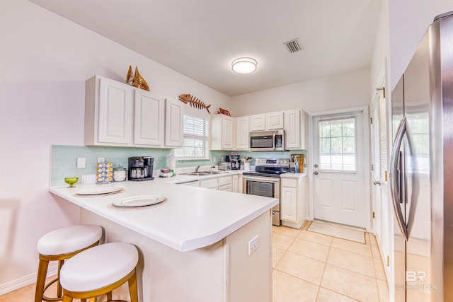 kitchen with appliances with stainless steel finishes, a kitchen bar, tasteful backsplash, plenty of natural light, and kitchen peninsula