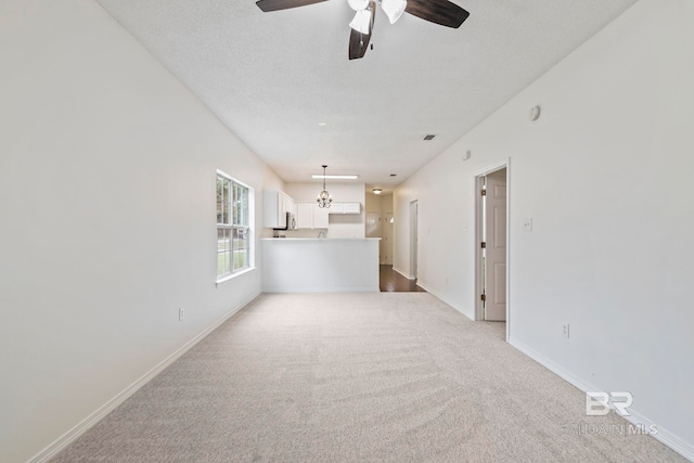 unfurnished living room featuring a textured ceiling, light carpet, and ceiling fan with notable chandelier