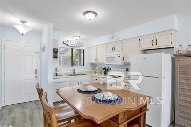 kitchen featuring white appliances, white cabinets, wood finished floors, light countertops, and a sink