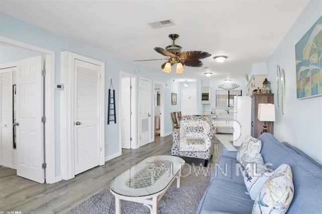 living area featuring a ceiling fan, baseboards, visible vents, and wood finished floors