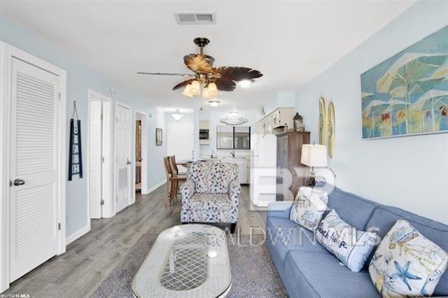 living area featuring a ceiling fan, visible vents, baseboards, and wood finished floors