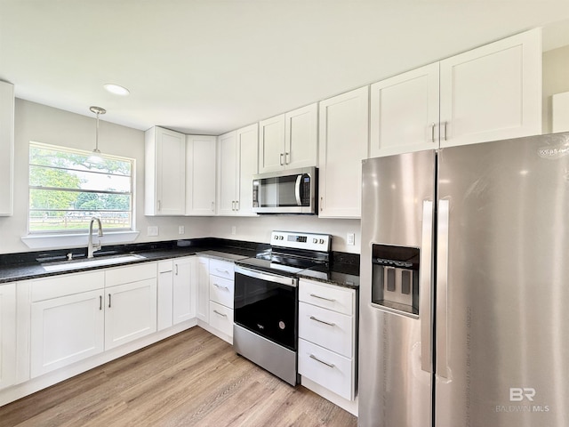 kitchen featuring white cabinets, a sink, light wood-style floors, stainless steel appliances, and decorative light fixtures