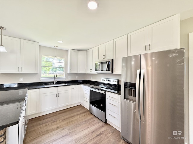 kitchen featuring a sink, stainless steel appliances, white cabinetry, pendant lighting, and dark countertops
