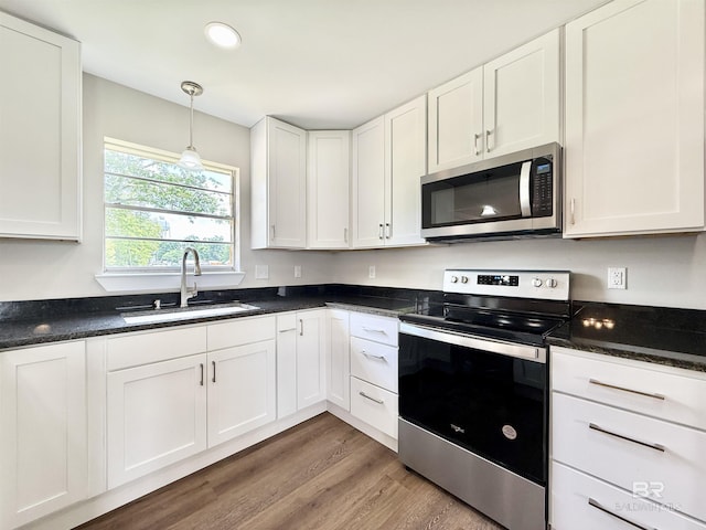 kitchen with white cabinetry, dark countertops, appliances with stainless steel finishes, and a sink