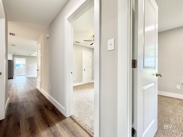 hallway with wood finished floors, visible vents, and baseboards