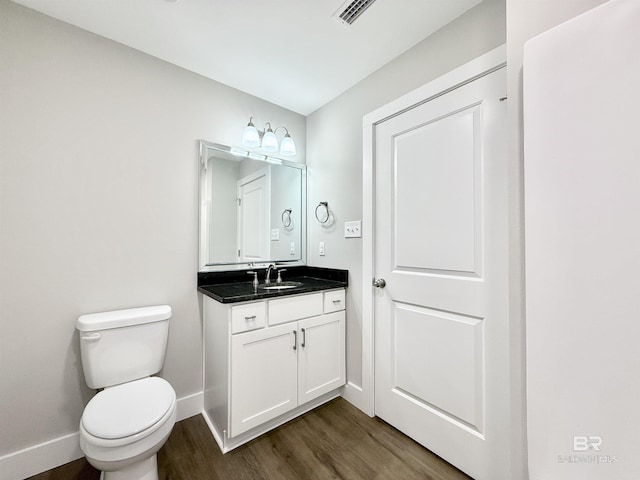 bathroom with wood finished floors, toilet, vanity, baseboards, and visible vents