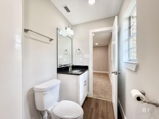 bathroom featuring visible vents, baseboards, toilet, wood finished floors, and vanity