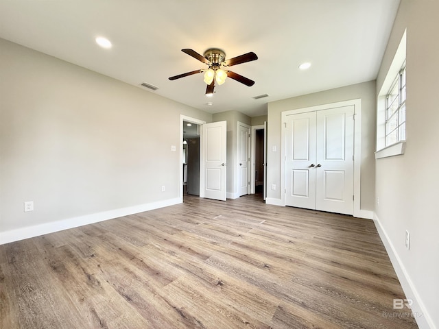 unfurnished bedroom with visible vents, multiple closets, wood finished floors, and baseboards