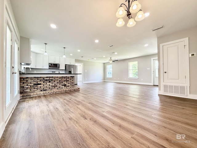 unfurnished living room with light wood finished floors, visible vents, baseboards, and ceiling fan with notable chandelier